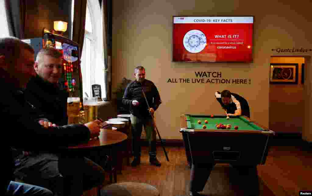 People play pool at a pub in Liverpool, Britain, as a television monitor shows news about the coronavirus outbreak.