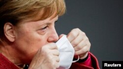 German Chancellor Angela Merkel puts on her face mask as she attends a session at the lower house of parliament Bundestag in Berlin, Germany, Dec. 9, 2020.