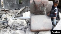 A boy holds a chair as he walks on the rubble of damaged buildings after an airstrike on the rebel-held town of Mesraba in the eastern Damascus suburb of Ghouta, Syria, Nov. 26, 2017. 