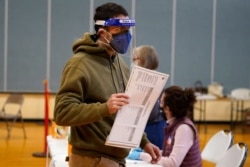 Julian St. Laurent wear a face shield and two face masks to help prevent the spread of the coronavirus as he walks to a voting both to cast his ballot to vote on Election Day, Nov. 3, 2020, in Portland, Maine.