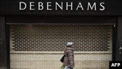 FILE - A woman walks past shutters at the entrance to a Debenhams department store in Manchester, April 4, 2020, as life in Britain continues during the nationwide lockdown to combat the novel coronavirus pandemic. 