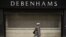 FILE - A woman walks past shutters at the entrance to a Debenhams department store in Manchester, April 4, 2020, as life in Britain continues during the nationwide lockdown to combat the novel coronavirus pandemic. 