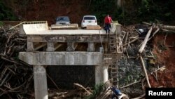 A woman looks as her husband climbs down a ladder at a partially destroyed bridge, after Hurricane Maria hit the area in September, in Utuado, Puerto Rico, Nov. 9, 2017.