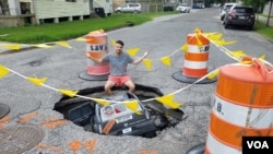 New Orleanian Joe Frisard sits beside a massive pothole two blocks from his home. Residents are no strangers to potholes, often decorating them or making jokes -- as was the case when someone placed a miniature car inside this one. (Matt Haines/VOA) 
