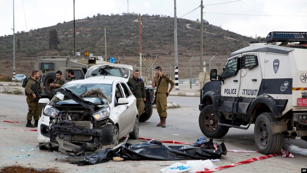 Tentara Israel dan polisi perbatasan berdiri dekat mayat seorang Palestina, tengah, yang menabrakkan mobilnya ke sekelompok orang Israel di Tepi Barat, dekat kota Palestina, Nablus, Minggu, 8 November 2015. Four Israelis were wounded from the incident and the attacker was shot dead by paramilitary officers, Israeli police said. (AP Photo/Ariel Schalit)