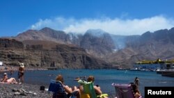 People watch a smoke from a forest fire on the Agaete beach in the village of Agaete, on the Canary Island of Gran Canaria, Spain, Aug. 20, 2019. 