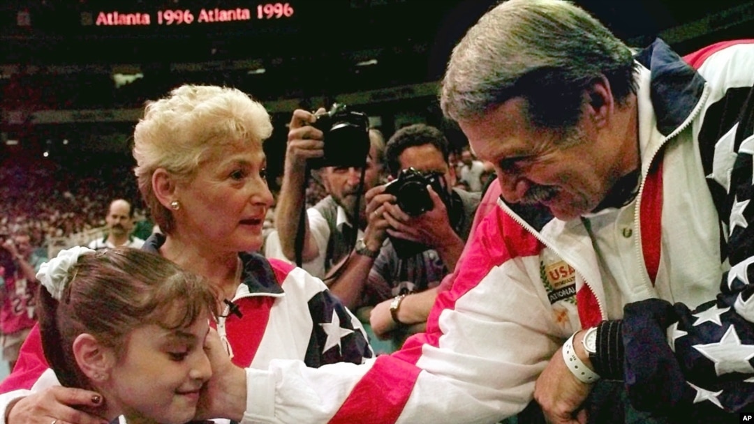 FILE - In this July 23, 1996, photo, Bela Karolyi, right, congratulates Dominique Moceanu, left, after the United States captured the gold medal in the women's team gymnastics competition at the Summer Olympic Games in Atlanta. U.S. team coach Martha Karolyi looks on. 