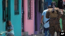 Una anciana observa cómo los soldados patrullan en la comunidad de San José del Pino en Santa Tecla, El Salvador, el miércoles 6 de abril de 2022, durante la represión sin precedentes del gobierno contra las pandillas.