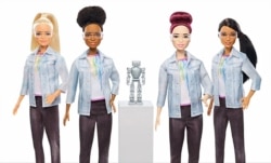 Four robotics engineer Barbies are seen flanked by a robot.