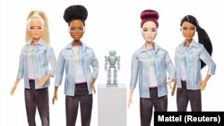 Four robotics engineer Barbies are seen flanked by a robot.