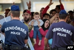 Hungarian police officers face a group of Syrian migrants, with a woman holding a baby, on the platform of the Kobanya-Kispest station, Budapest suburb, on Sept. 2, 2015, as the refugees refused to board a train to the Debrecen camp.