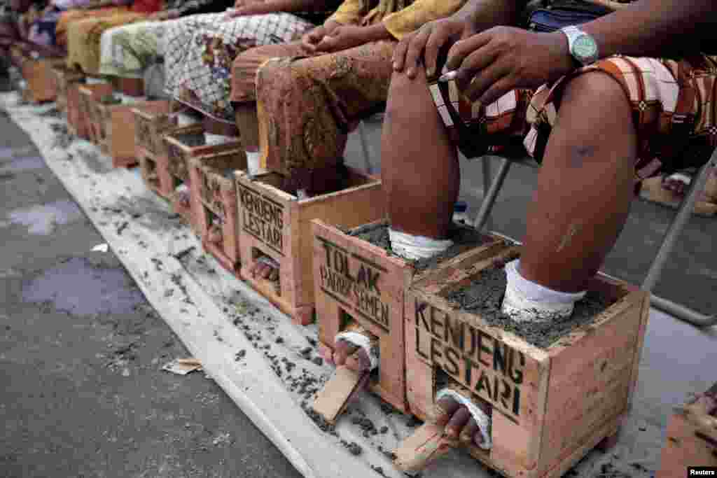 Villagers whose feet are cast in cement blocks sit on a bench as part of a four-day protest to draw attention to what they say is environmental damage to their farmland from a cement factory, in Rembang, Central Java, outside the presidential palace in Jakarta, Indonesia.