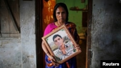 Fatema holds a picture of her son Nurul Karim as she poses for a photograph in front of her house in Savar, April 21, 2014. Fatema lost her son and her daugther Arifa, who were working at the Rana Plaza when it collapsed on April 24, 2013.