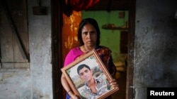 Fatema holds a picture of her son Nurul Karim as she poses for a photograph in front of her house in Savar, April 21, 2014. Fatema lost her son and her daugther Arifa, who were working at the Rana Plaza when it collapsed on April 24, 2013.