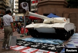 A shopper in Hong Kong stands in front of a model tank made by university students to remember the crackdown in Tiananmen Square, June 3, 2014.