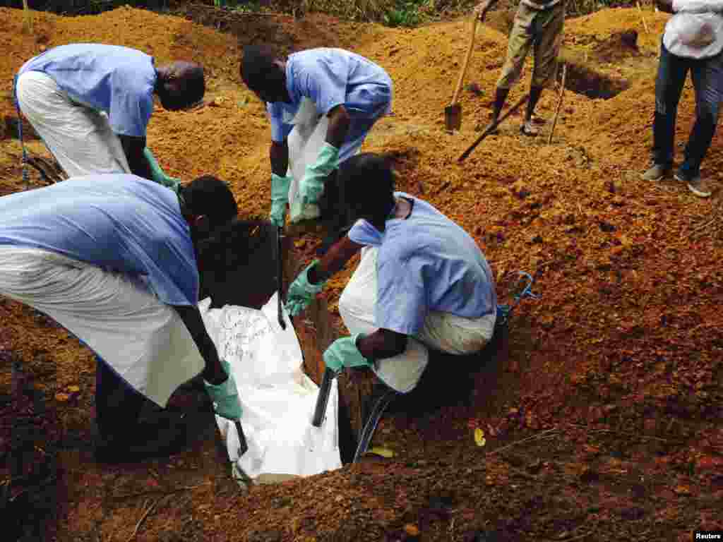 Volunteers lower a corpse into a grave. They are using safe burial practices to reduce person-to-person transmission of Ebola, in Kailahun, Eastern Province of Sierra Leone, Aug. 2, 2014.