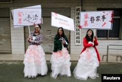 FILE - University students dressed as battered wives hold banners in front of an office of China's Civil Affairs department, where local people register for marriage, in protest of domestic violence, during the International Day for the Elimination of Violence against Women, in Hubei province, Nov. 25, 2012.