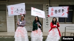 FILE - University students dressed as battered wives hold banners in front of an office of China's Civil Affairs department, where local people register for marriage, in protest of domestic violence, during the International Day for the Elimination of Violence against Women, in Hubei province, Nov. 25, 2012. 