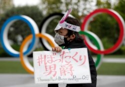 Pengunjuk rasa anti-Olimpiade memamerkan plakat di depan monumen cincin Olimpiade. (Foto: REUTERS/Issei Kato)