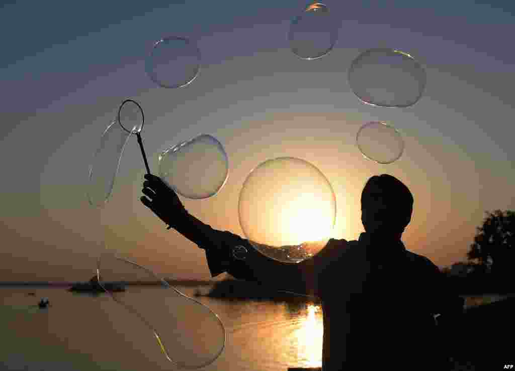 A silhouetted Pakistani vendor forms bubbles while waiting for customers at a stall selling bubbles and balloons at the Rawal Lake park in Islamabad.