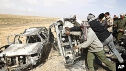 Rebel fighters push cars burnt in what they say was a coalition airstrike on a group of vehicles killing around ten on the road between Ajdabiyah and Brega, in Libya, April 2, 2011