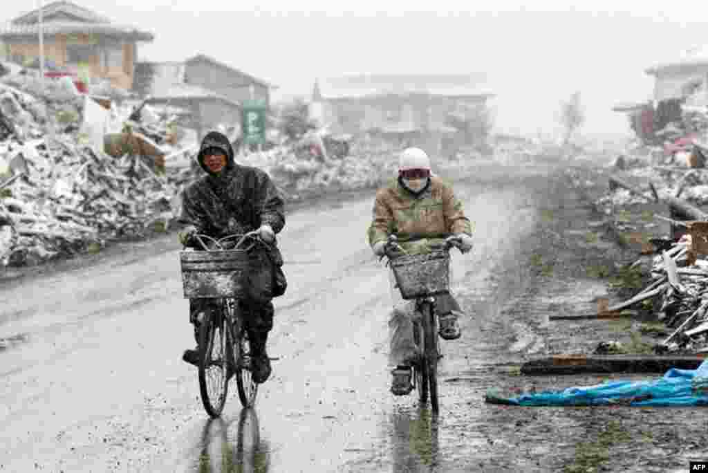 March 17: People ride bicycles past houses destroyed by an earthquake and a tsunami as snow falls in Natori City, Japan. (Reuters/Kyodo )