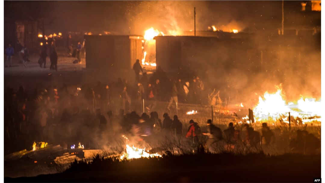 FILE - Migrants evacuate as a huge fire blazes through the Grande-Synthe migrant camp outside the northern French city of Dunkirk late April 10, 2017, reducing it to "a heap of ashes," the regional chief said.