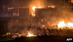 Migrants evacuate as a huge fire blazes through the Grande-Synthe migrant camp outside the northern French city of Dunkirk late April 10, 2017, reducing it to "a heap of ashes," the regional chief said.
