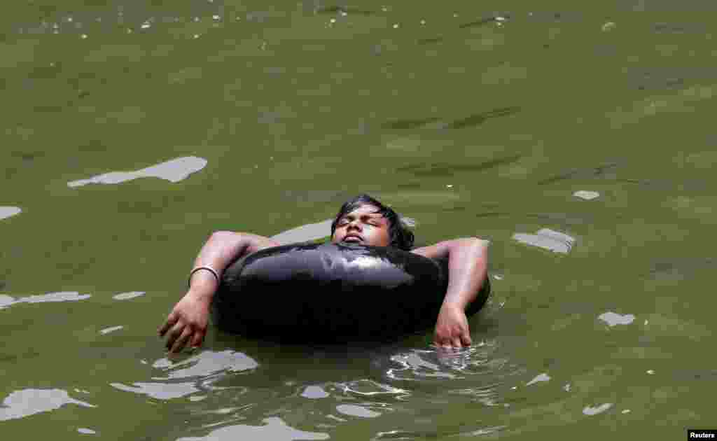 Seorang anak laki-laki menggunakan ban untuk berenang di sebuah danau buatan di dalam kuil suci di New Delhi, India.