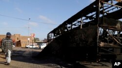 Un homme passe devant un bus brûlé lors des émeutes, à Atteridgeville, Pretoria, 22 juin, 2016. (AP Photo / Themba Hadebe)