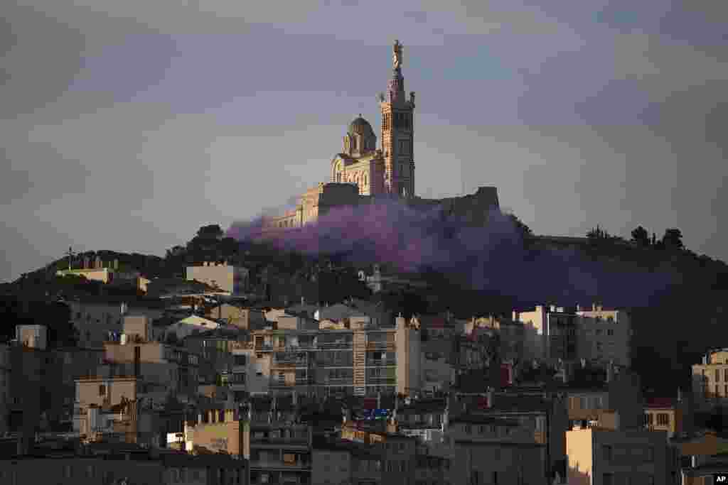 Para seniman dan pekerja seni menyalakan asap berwarna untuk menuntut lebih banyak dukungan dari pemerintah setelah pandemi menghancurkan pendapatan mereka, di depan basilika Notre-Dame de la Garde di Marseille, Prancis selatan (28/5) (Foto: AP).&nbsp;