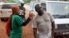 FILE - A health worker uses a thermometer to screen a man at a makeshift road block run by Guinean security forces outside the town of Forecariah, Guinea.