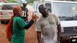 Health worker, left, uses a thermometer to screen a man at a makeshift road block run by Guinean security forces outside the town of Forecariah, Guinea, Sept. 7, 2014.