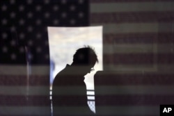FILE - Hal Pigg is reflected in an image of a flag, as he casts his vote on Election Day in Jamul, California, Nov. 6, 2012.