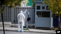 FILE - Forensic experts search the area outside the Russian Consulate in Athens in the wake of an explosion, March 22, 2019. On April 18, 2019, a Greek anarchist group claimed responsibility for exploding a grenade at the site. 
