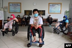 Siswa dan terapis mengenakan masker menunggu di aula, sementara anggota Palang Merah Indonesia mendisinfeksi sekolah untuk anak-anak cacat, di tengah kekhawatiran tentang virus COVID-19, di Jakarta.18 Maret 2020. (Foto: ADEK BERRY / AFP)