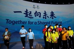 Attendees pose for pictures in front of a giant screen showing the slogan for the Beijing 2022 Winter Olympic Games, "Together for a shared future", following a ceremony in Beijing, China, Sept. 17, 2021.