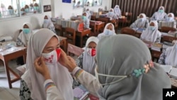 Seorang pejabat kesehatan masyarakat menunjukkan cara memakai masker yang benar kepada siswa di Pondok Pesantren Daarul Rahman, Jakarta, Rabu, 18 November 2020. (Foto AP / Tatan Syuflana)