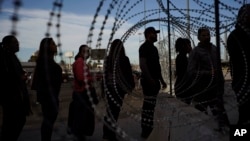 Pedestrians stand near barbed wire at a legal Mexico-U.S. border crossing as they prepare to leave Tijuana, Mexico, Monday, Nov. 19, 2018. (AP Photo/Ramon Espinosa)