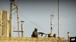 In this undated citizen journalism image made on a mobile phone and acquired by the AP, Syrian soldiers stand on the roof of a building in an undisclosed location in Syria