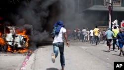 Manifestantes corren después que automóviles fueran incendiados cerca de un hotel Best Western durante protestas por el aumento en los precios de la gasolina en Puerto Príncipe, Haití, el sábado, 7 de julio de 2018.