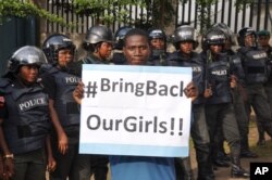 FILE - A man poses with a sign in front of police officers in riot gear during a demonstration calling on the government to rescue the kidnapped girls of the government secondary school in Chibok, in Abuja, Nigeria, Oct. 14, 2014.