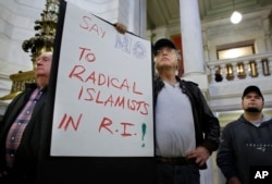 FILE - Howard Brown, of North Kingstown, R.I., center, displays a placard during a rally at the statehouse in Providence, R.I., held to demonstrate against allowing Syrian refugees to enter Rhode Island, Nov. 19, 2015.