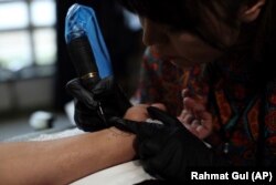 In this Saturday, November 9, 2019, photo, Suraya Shaheedi, 26, Tattoo artist, right, pierced tattoo to a male customer in Kabul, Afghanistan.