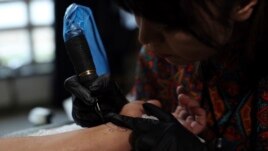 In this Saturday, November 9, 2019, photo, Suraya Shaheedi, 26, Tattoo artist, right, pierced tattoo to a male customer in Kabul, Afghanistan.