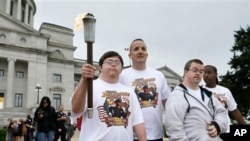 David Dallas, left, carries the Arkansas Special Olympics Torch accompanied by Little Rock police Capt. Heath Helton, center, and other athletes at the Arkansas state Capitol in Little Rock, Ark., May 21, 2015.