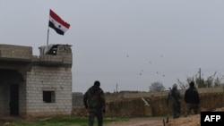 A Syrian national flag is seen flying over a building as regime forces gather in the southern countryside of the northern Kurdish-controlled city of Manbij, Dec. 30, 2018.