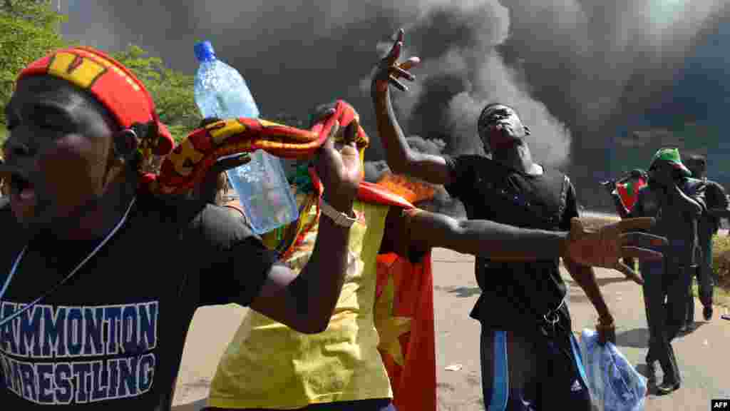 Les manifestants se tiennent devant le parlement où des voitures et des documents brulent, à Ouagadougou le 30 Octobre, 2014. Des centaines de manifestants en colère au Burkina Faso ont pris d&#39;assaut le parlement le 30 Octobre avant d&#39;y mettre le feu en signe de protestation contre l&#39;intention de modifier la Constitution pour permettre au Président Blaise Compaoré pour étendre son règne de 27 ans. AFP PHOTO / ISSOUF SANOGO 