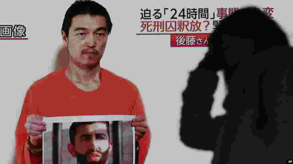 A passerby is silhouetted against a large TV broadcasting a news program showing a still photo of Japanese hostage Kenji Goto holding what appears to be a photo of Jordanian pilot Mu'ath al-Kaseasbeh, in Tokyo, Jan. 28, 2015.