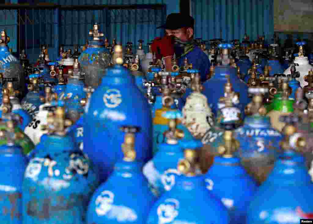 An employee adjusts a scarf on his face as he walks near oxygen cylinders at a factory amid the coronavirus outbreak in Jakarta, Indonesia.